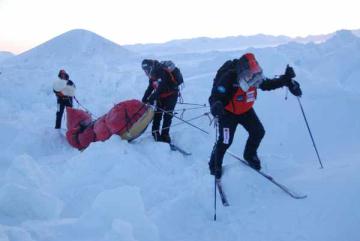 Toni wrestles with pack ice, assisted by team members. Ward Hunt Island can be seen in the background.